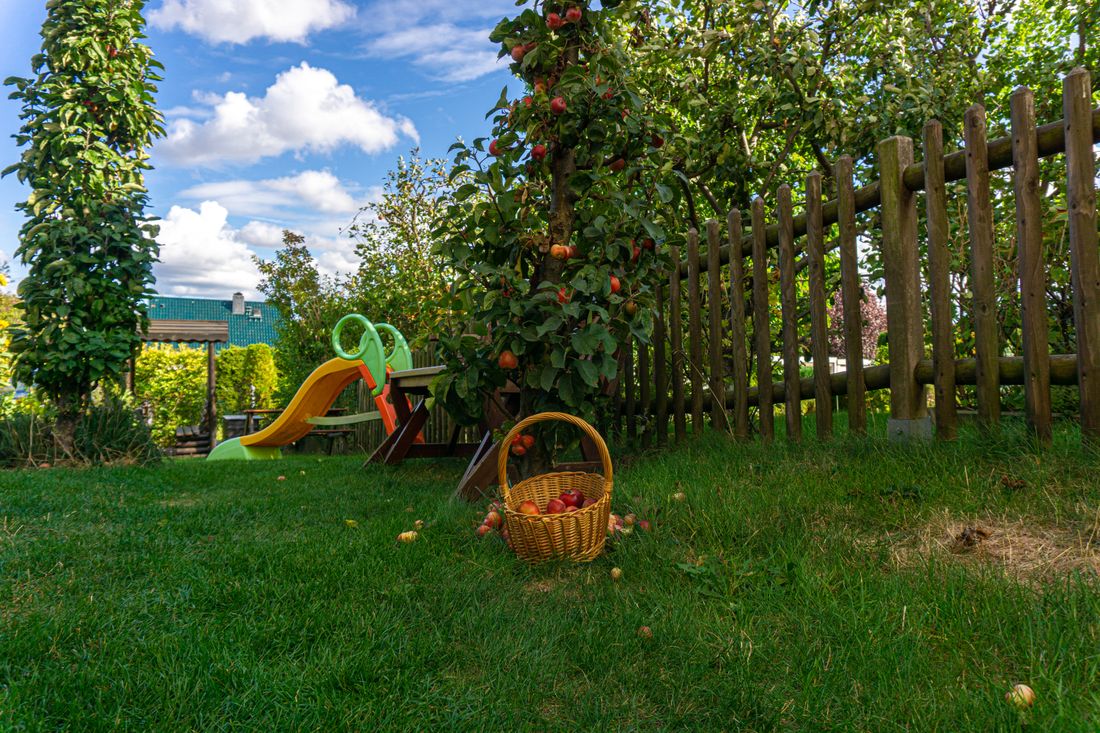Garten mit Rutsche, Kindertisch, Apfelbäumen und einem Korb voller Äpfel auf der Wiese