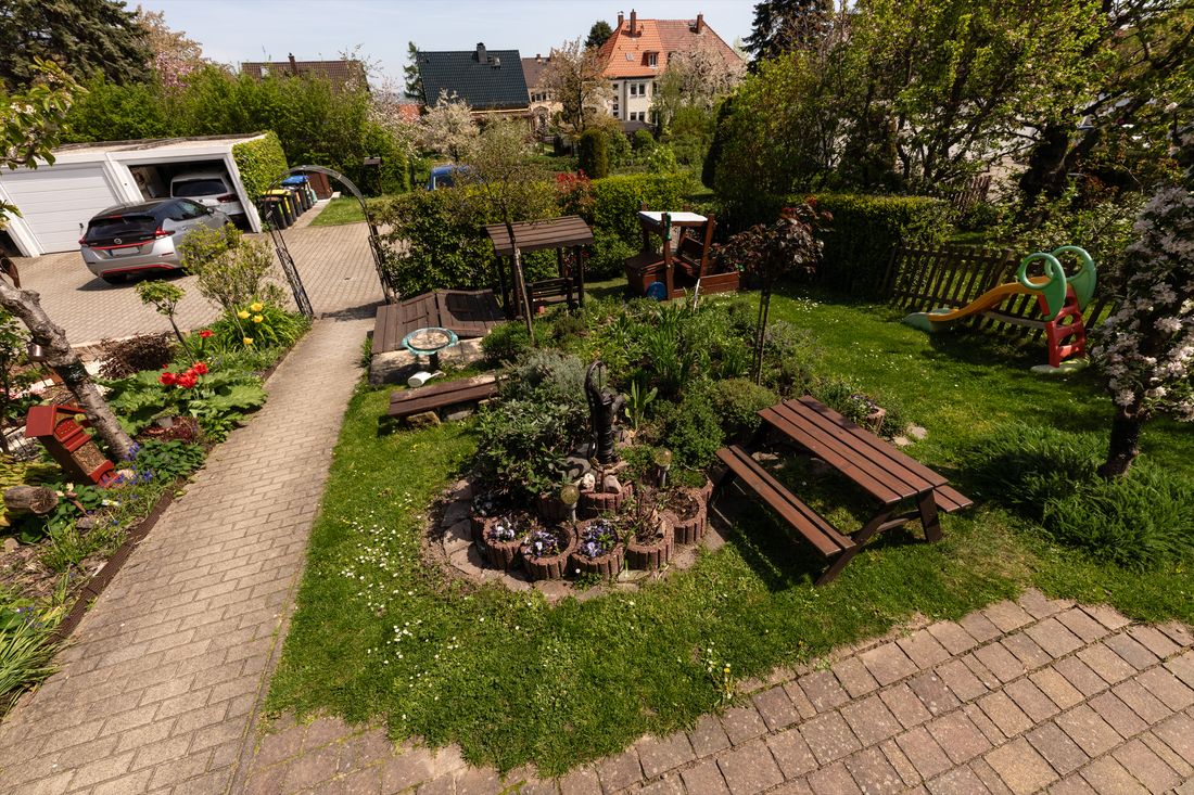 Blick von oben auf den großen Garten mit Wiese, Picknicktisch, Rutsche und Kräuterbeet